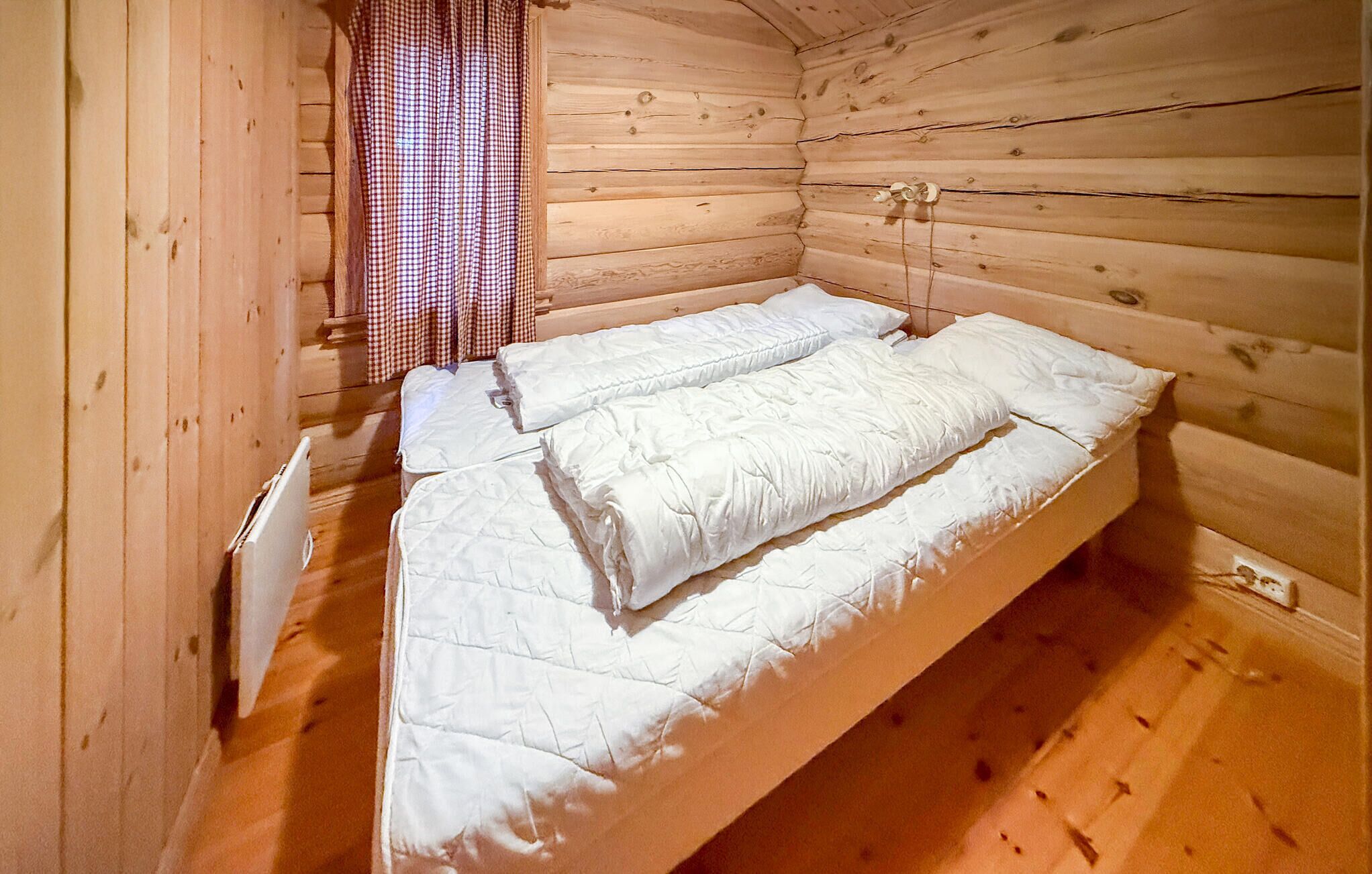 Una cama individual con ropa de cama blanca en una habitación tipo cabaña de madera.