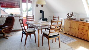 Un coin repas avec une table dressée pour quatre personnes, des chaises en bois, un radiateur, un poêle et un meuble avec des tiroirs.