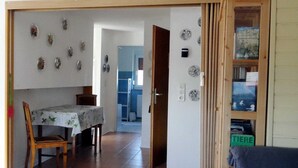 Un coin repas avec une table et des chaises, une cuisine à l’arrière-plan et une porte donnant sur une autre pièce.