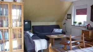 Un salon chaleureux avec un canapé bleu foncé, un meuble en bois doté de portes en verre, une petite télévision et un coin repas comprenant une table et des chaises.