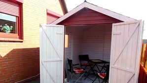 Un petit abri ouvert, avec un toit rouge et des murs blancs, contenant une table et des chaises.