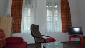 Una sala de estar con un sofá rojo, un sillón marrón, una mesa de centro de vidrio y un televisor sobre un soporte rojo.