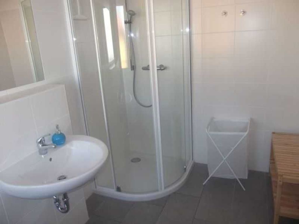 Une salle de bain avec une douche à parois de verre, un lavabo blanc et une petite poubelle blanche.