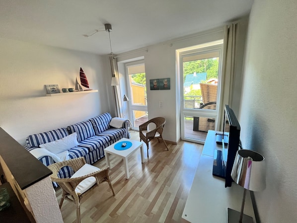 A living room with a striped sofa, a small table, wicker chairs, a TV, and a view of the outdoors through a sliding glass door. - Zempin Ostseepark WE 34 Island Usedom only 150m to the beach - WE 34 (Zempin)