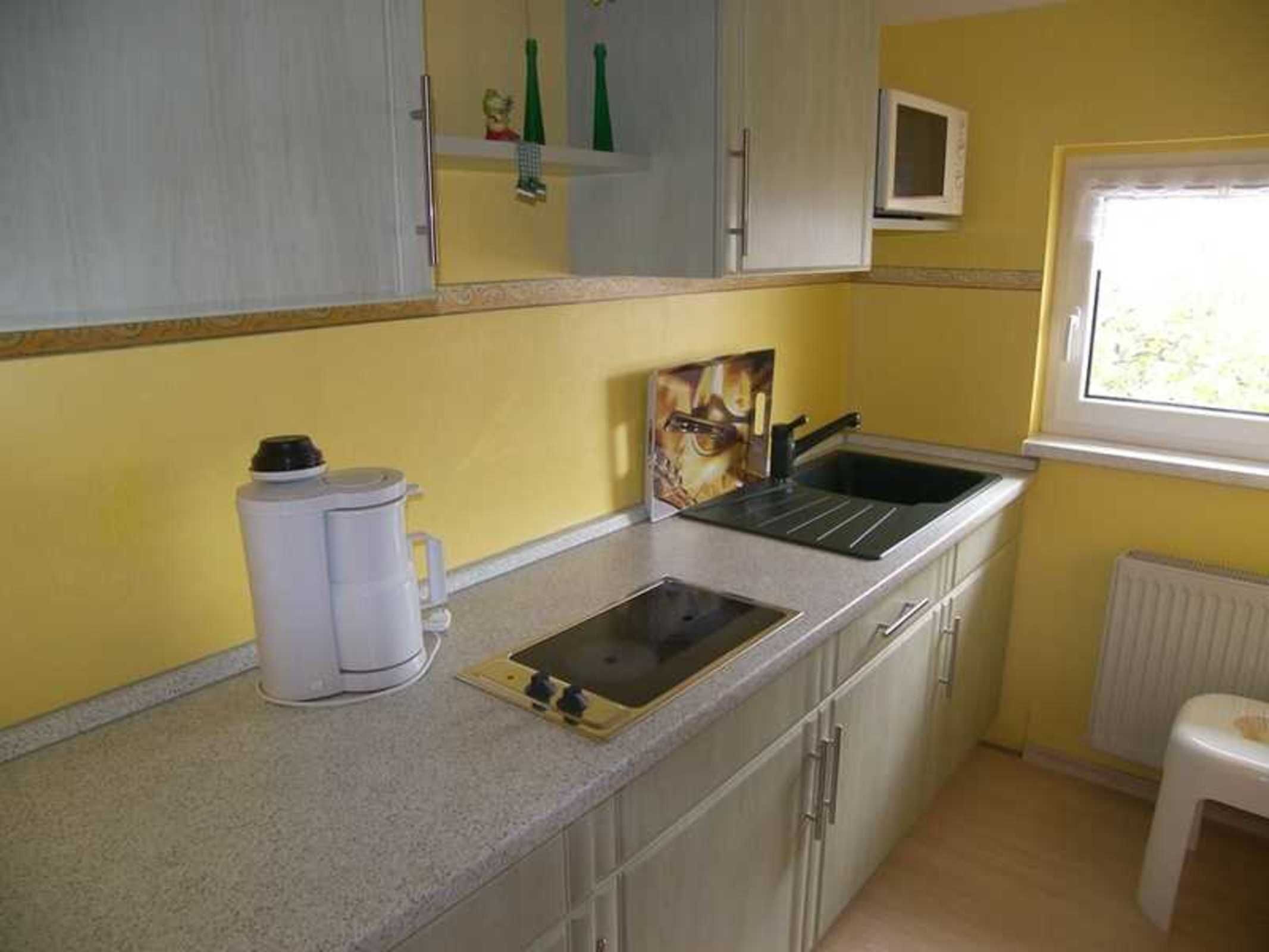 Una cocina compacta con un lavamanos, una cafetera y una ventana.
