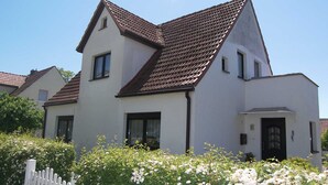 A two-story house with a sloped roof, white exterior walls, and a white picket fence. - Apartment 02 - Apartments Oechsner (Heringsdorf)