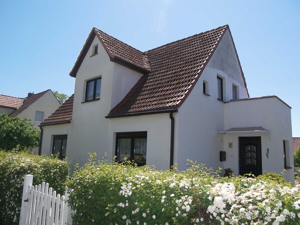 A two-story house with a sloped roof, white exterior walls, and a white picket fence.