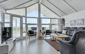 A spacious room with a large glass door leading to a balcony, a black leather sofa, a wooden coffee table, and a television on a white cabinet. - Beautiful home in Nordborg with WiFi (Nordborg)