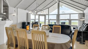 Ruime eethoek met hoge plafonds en grote ramen, houten stoelen, een ronde tafel en uitzicht op de omgeving.