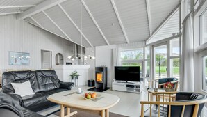 Een moderne woonkamer met een zwarte leren bank, een ronde salontafel met fruit, een televisie en een open haard.