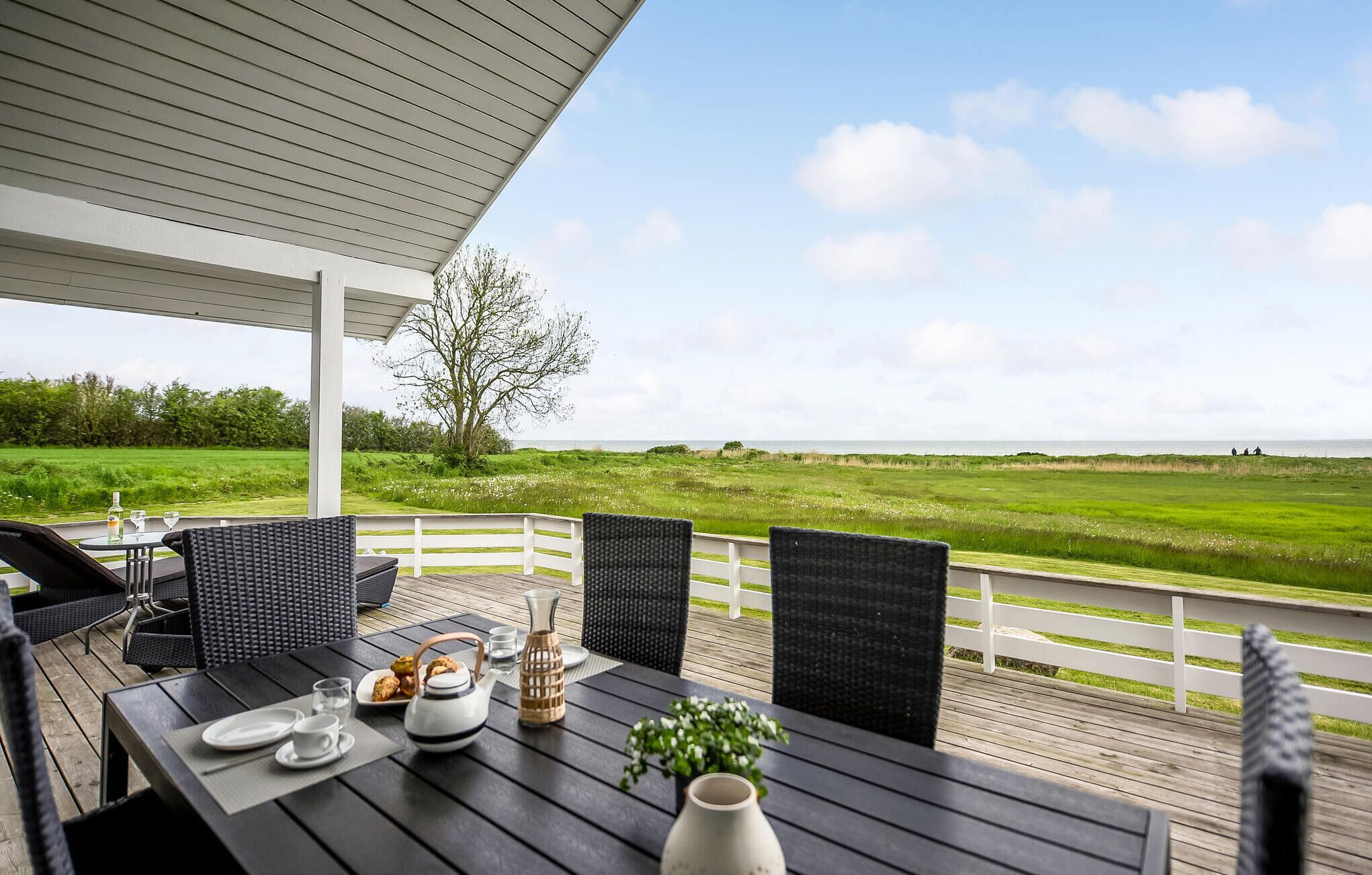 Un espace extérieur aménagé, abrité et doté d’une table pour deux, offrant une vue sur un paysage verdoyant et la mer.