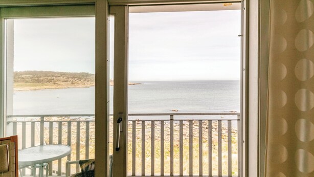 Ein Zimmer mit Meerblick durch eine Glastür, ein Balkon mit Geländer und ein kleiner Tisch mit Stühlen.