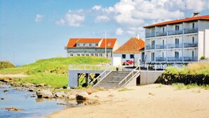 Ein Hotel an der Küste mit einer Brücke zum Strand, das mehrere Balkone und ein Gebäude mit rotem Dach zeigt.