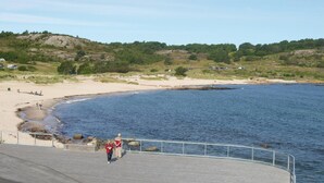 Eine Küstenlandschaft mit Sandstrand, felsiger Küste und einem befestigten Weg zum Wasser.