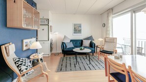 Ein modernes Wohnzimmer mit einem blauen Sofa, Holzstühlen, einem Esstisch und einer Küchenzeile mit Mikrowelle und Kühlschrank.