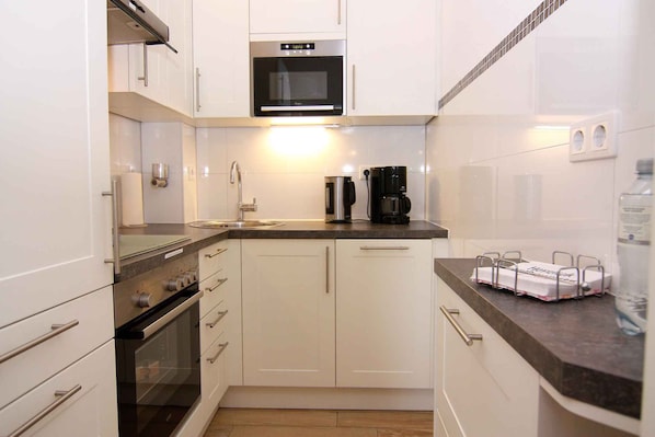 A compact kitchen with white cabinets, a microwave, a coffee maker, and a sink.