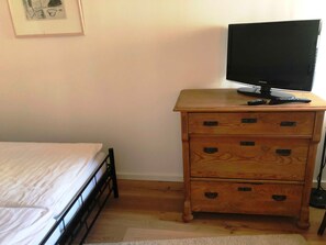 Ein Schlafzimmer mit einem Bett, einer Holzkommode mit Schubladen, einem Fernseher darauf und einem gerahmten Bild an der Wand.