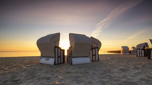 Beach chairs arranged on a sandy beach with a sunset in the background.