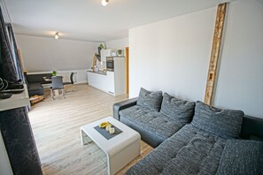 Un salon moderne avec un canapé gris, une petite table basse blanche et une cuisine en arrière-plan.