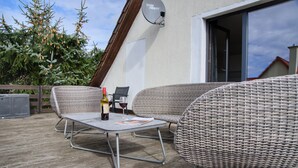 An outdoor patio with wicker furniture, a table with a bottle and glass, and a satellite dish on the wall.
