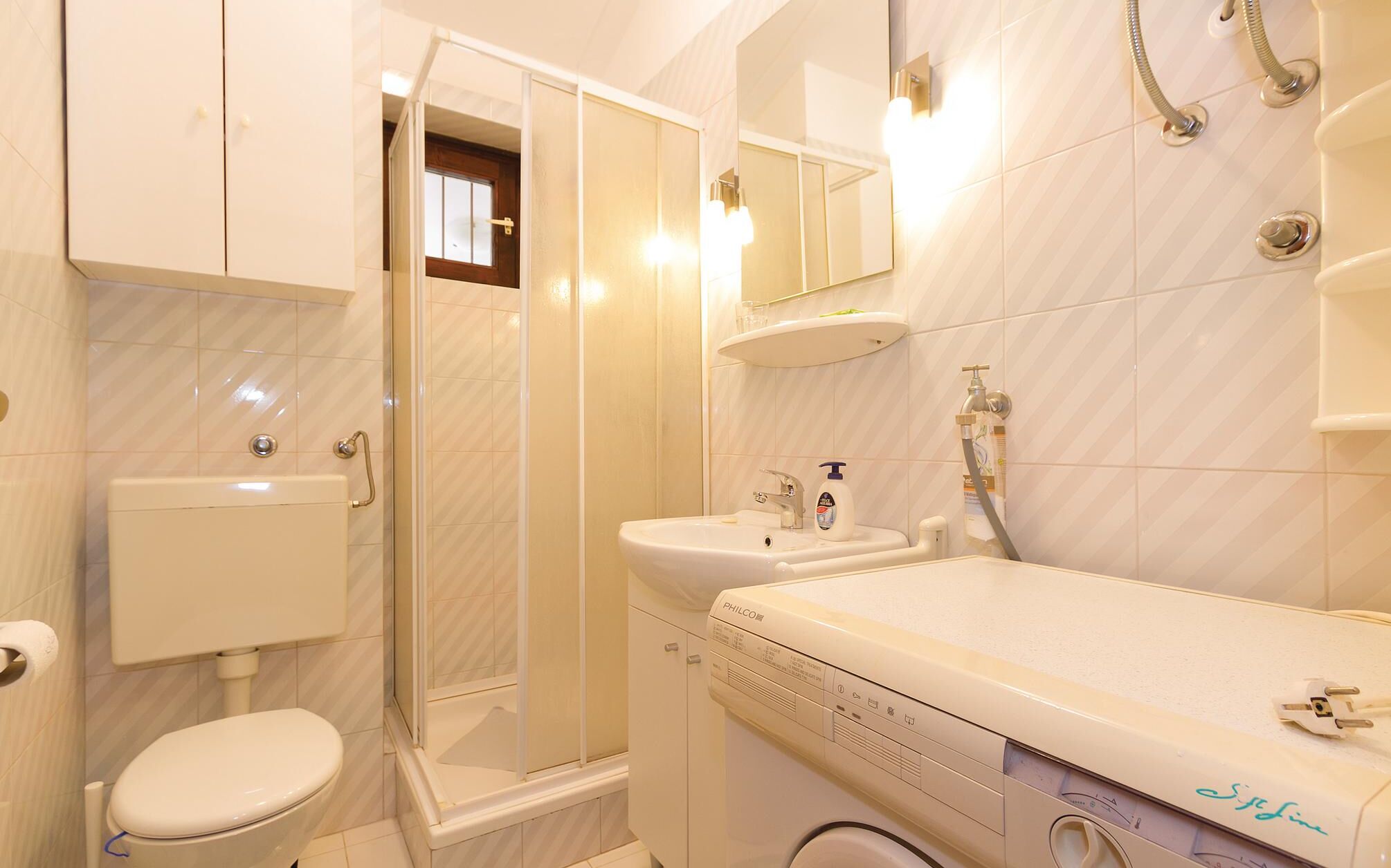Een moderne badkamer met toilet, douche, wastafel en een wasmachine.