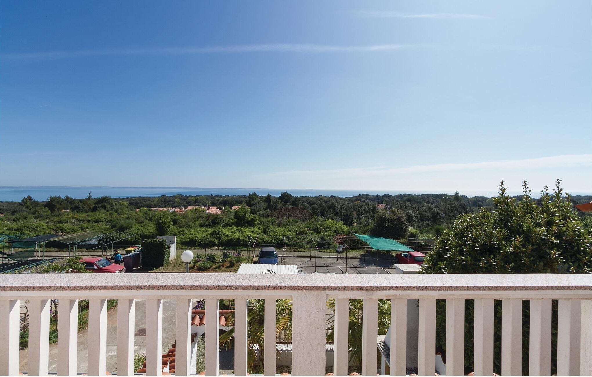 A balcony with a view of a coastal landscape, including trees, a clear sky, and distant hills.