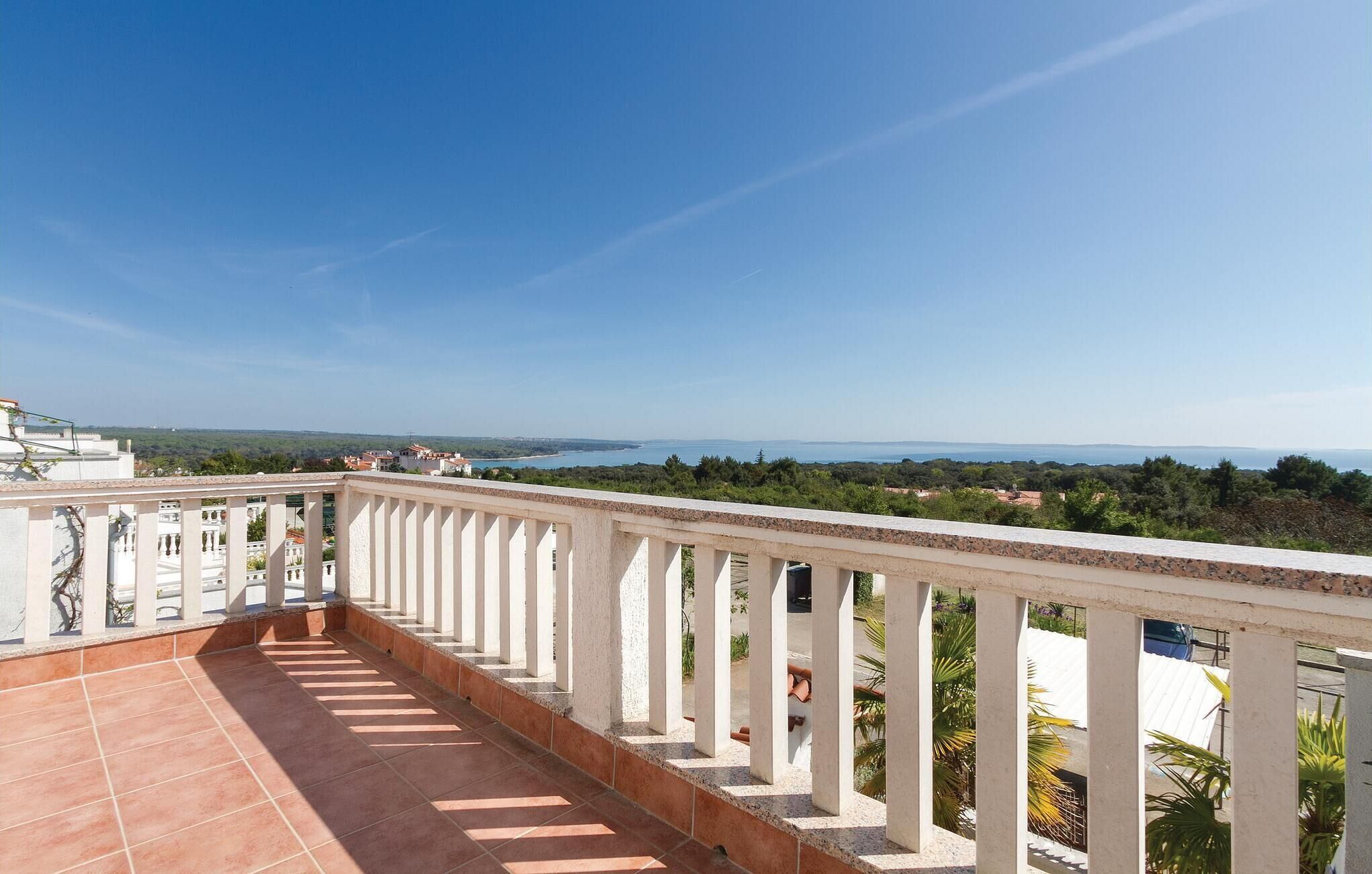 Un balcon offrant une vue sur un paysage côtier, comprenant une étendue d’eau et des collines lointaines.
