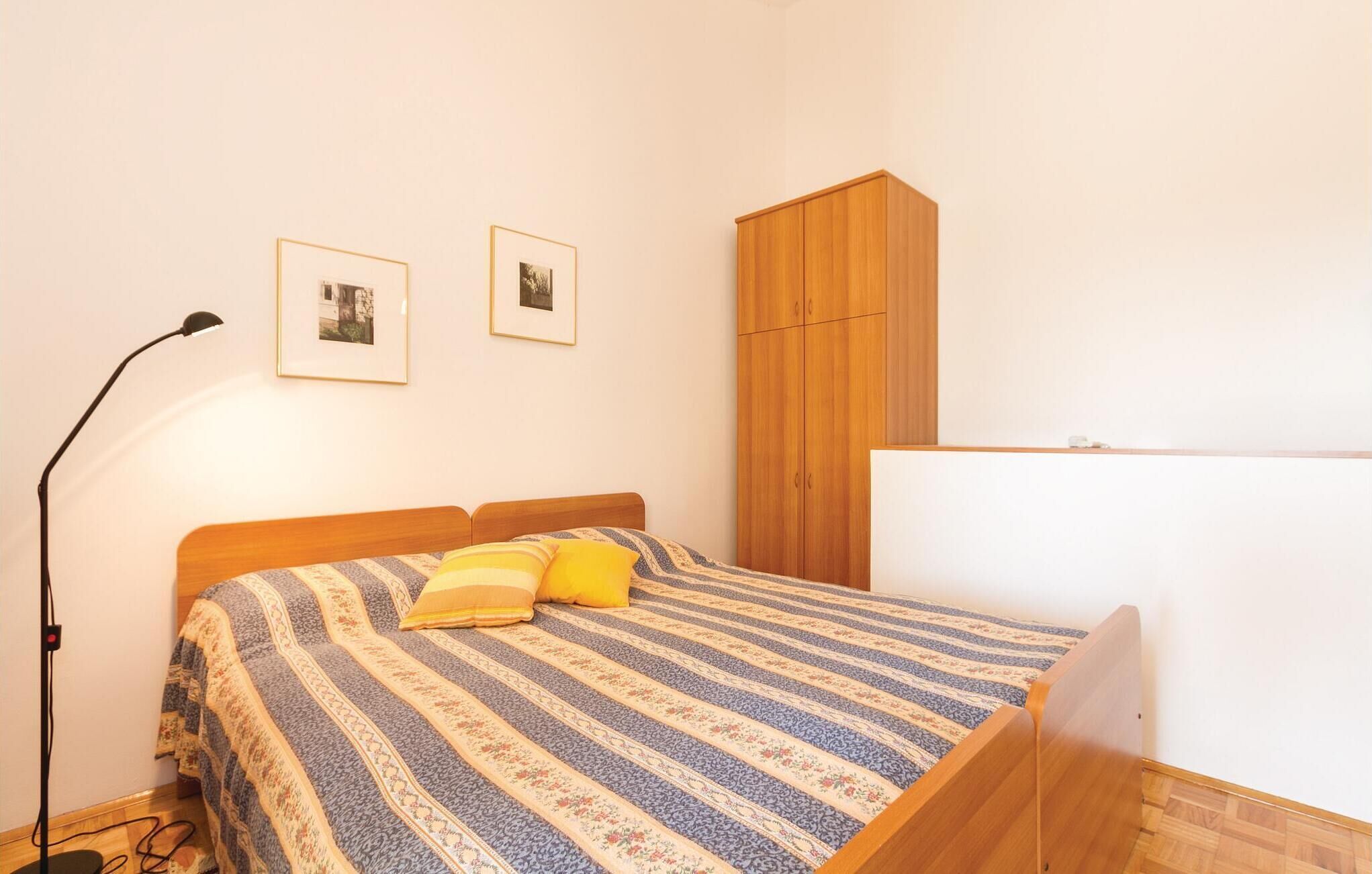 Un dormitorio con cama, armario de madera, lámpara de pie y dos cuadros en la pared.