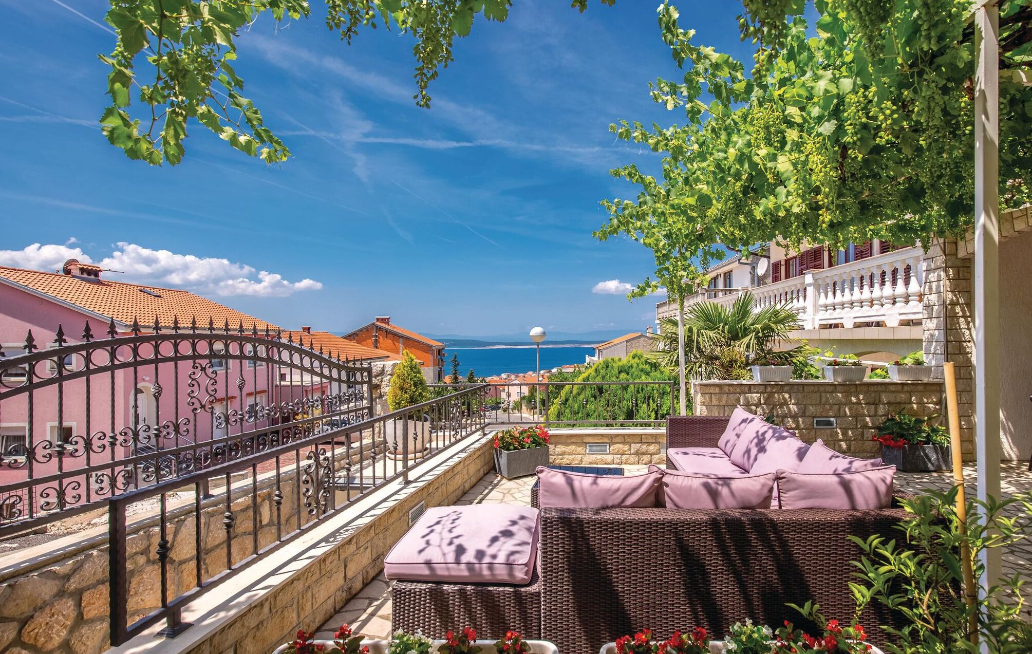 A balcony with wicker furniture, a view of the sea, and a stone wall.