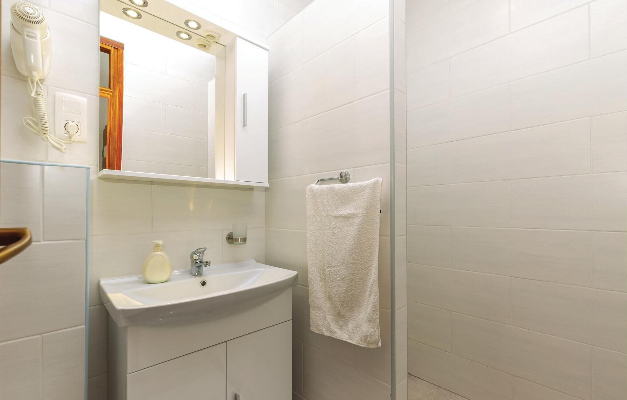Un baño con lavamanos blanco, espejo, toallero y secador de pelo.