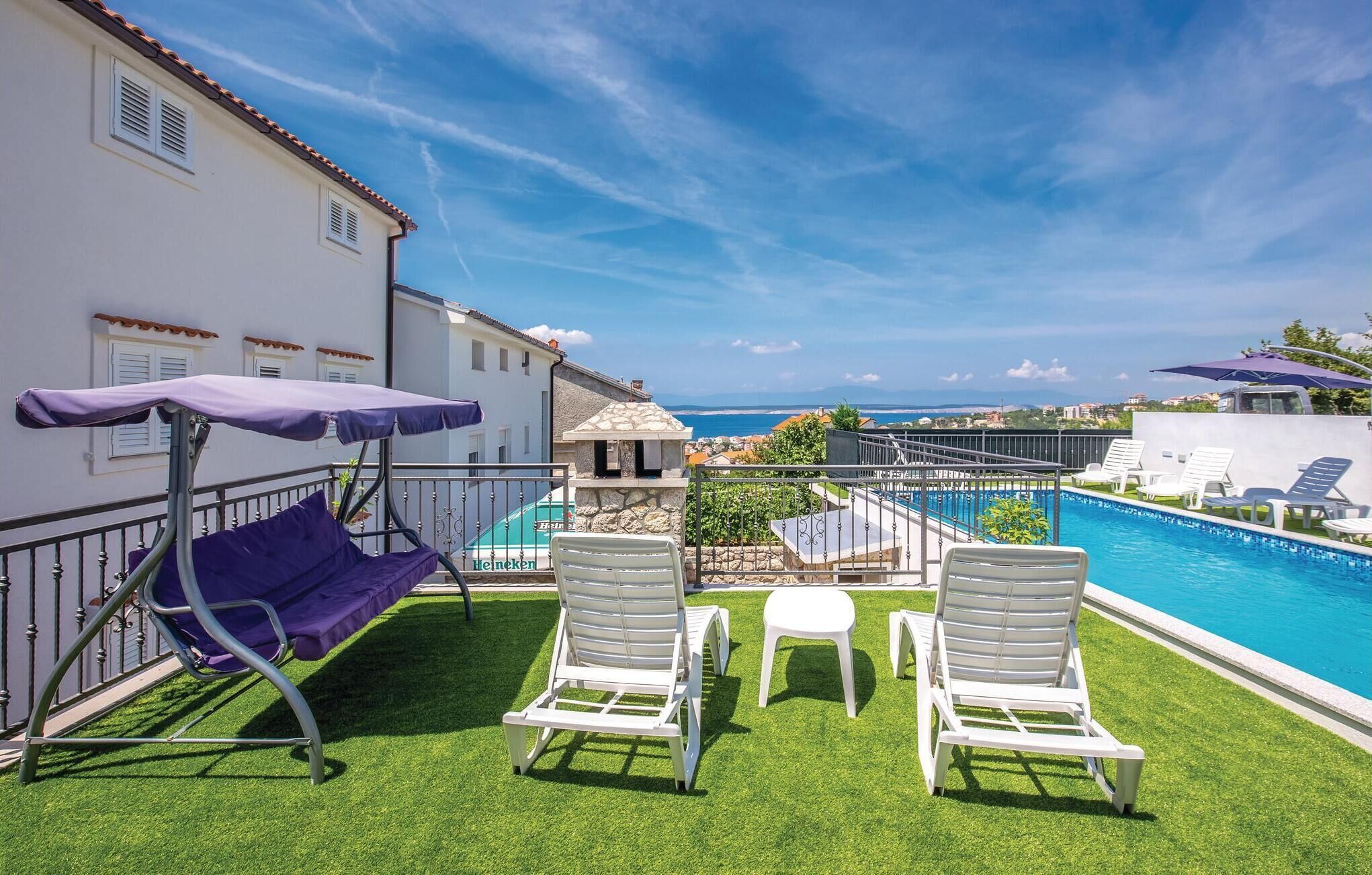 A poolside area with a view of the sea, two white lounge chairs, a purple umbrella, and a small table.