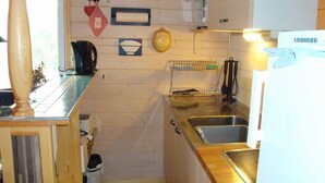 Eine kleine Küche mit Holzwänden, einem Spülbecken, einem Wasserkocher und einem Geschirrgestell.