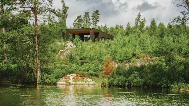 A modern house with a flat roof, surrounded by dense forest and a body of water. - Beautiful home in Holmsjö with WiFi (Holmsjö)