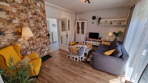 A modern living room with a stone wall, wooden flooring, a sofa, a yellow armchair, and a hanging chair.