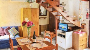 Zona de menjador amb taula de fusta preparada per a dues persones, una ampolla de vi i un vas amb flors. Hi ha un televisor fixat a la paret, i se'n veu una escala de fusta al fons.
