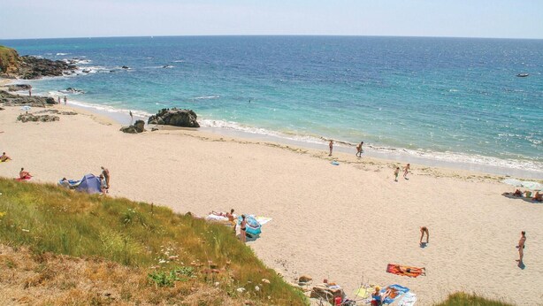 Una platja amb aigua turquesa i sorra daurada, i gent gaudint del dia.