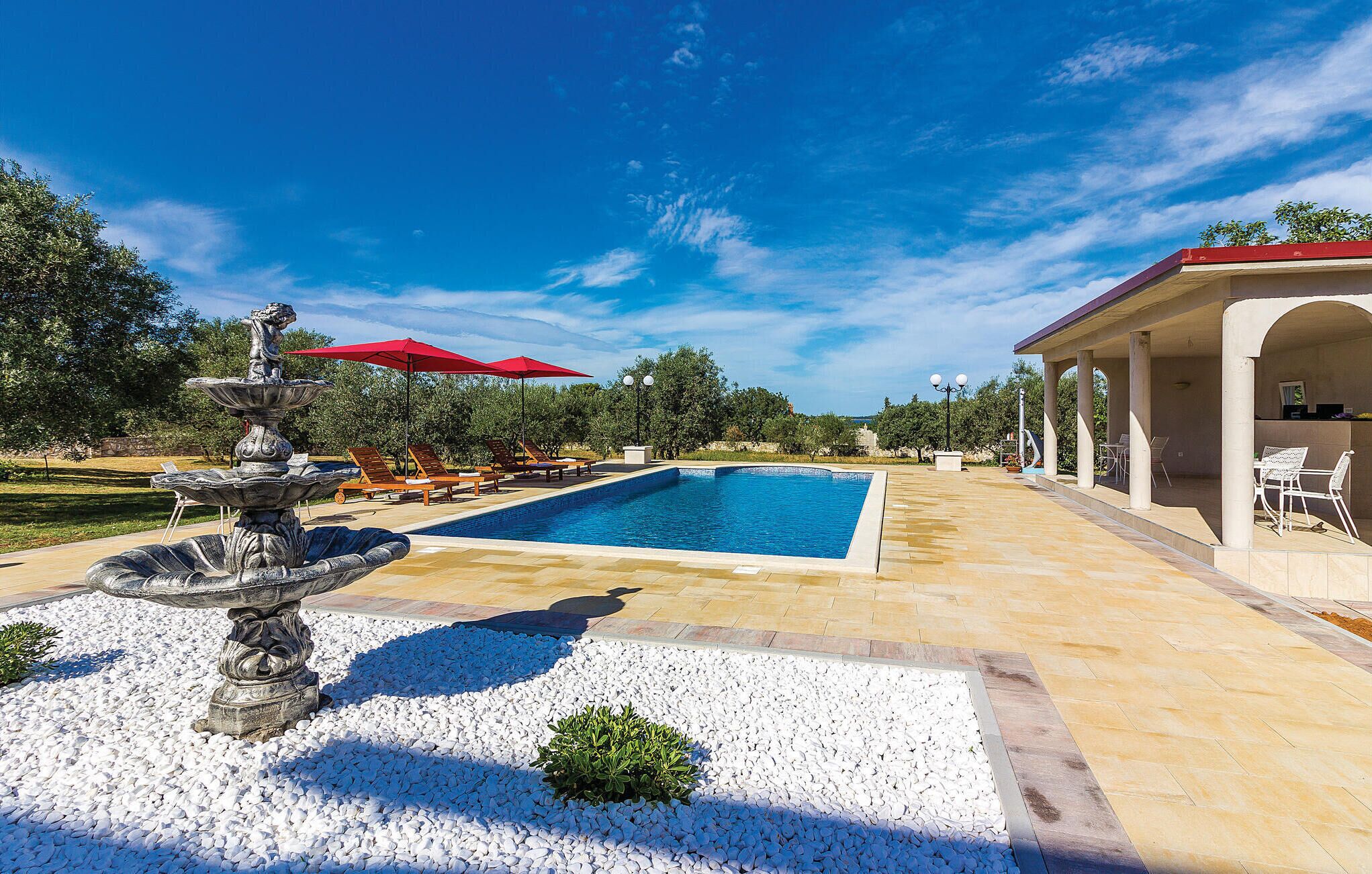 Une piscine avec une fontaine, des chaises longues et un patio couvert.