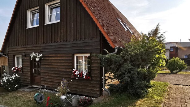 Ett trähus med ett brant tak, två fönster och en liten veranda med krukväxter.