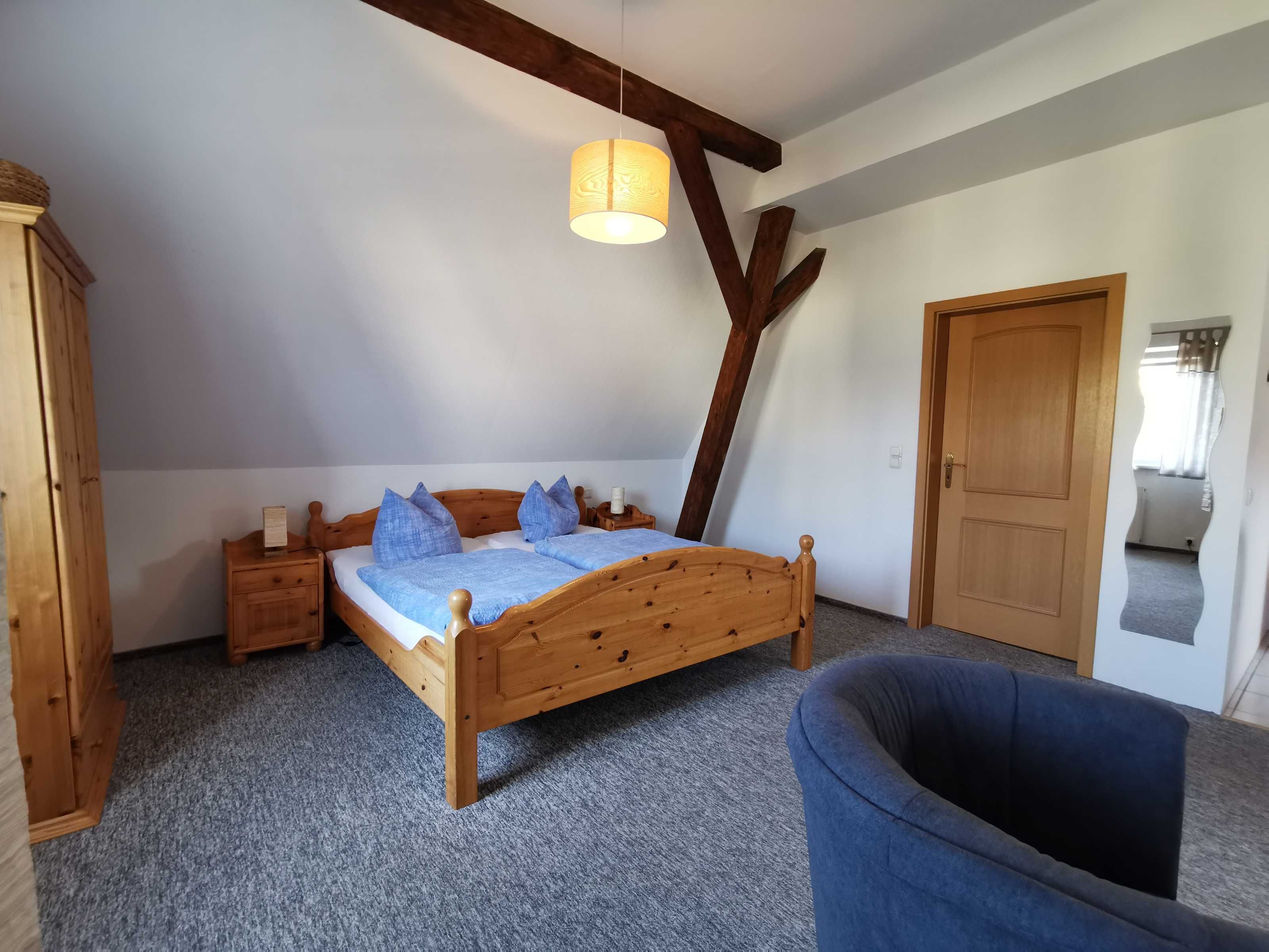 A bedroom with a wooden bed, a nightstand, a wardrobe, and a mirror.