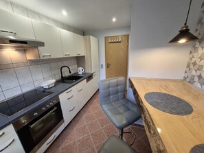 A modern kitchen with white cabinets, a black countertop, a built-in oven, and a wooden dining table with a bench.