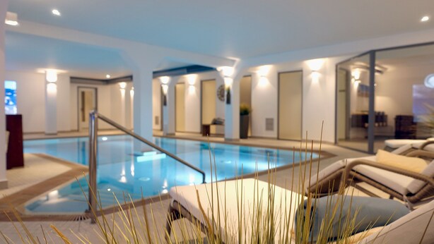 Una piscina interior moderna con sillones de descanso y una barrera de cristal.