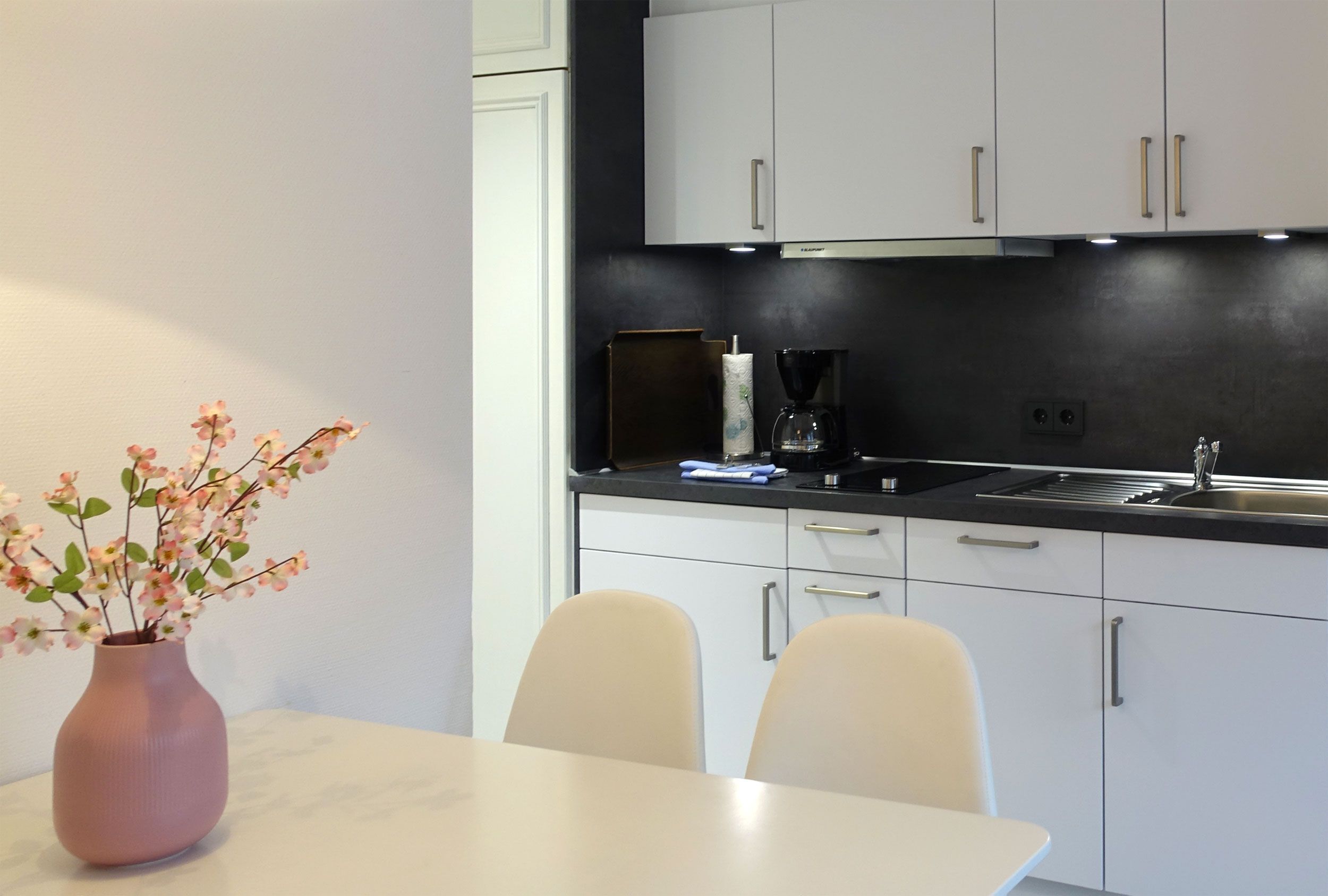 Eine moderne Küche mit weißen Schränken, einer schwarzen Arbeitsplatte und einem Tisch mit Blumen in einer Vase.