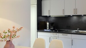 Una cocina moderna con armarios blancos, una encimera negra y un florero con flores sobre una mesa.