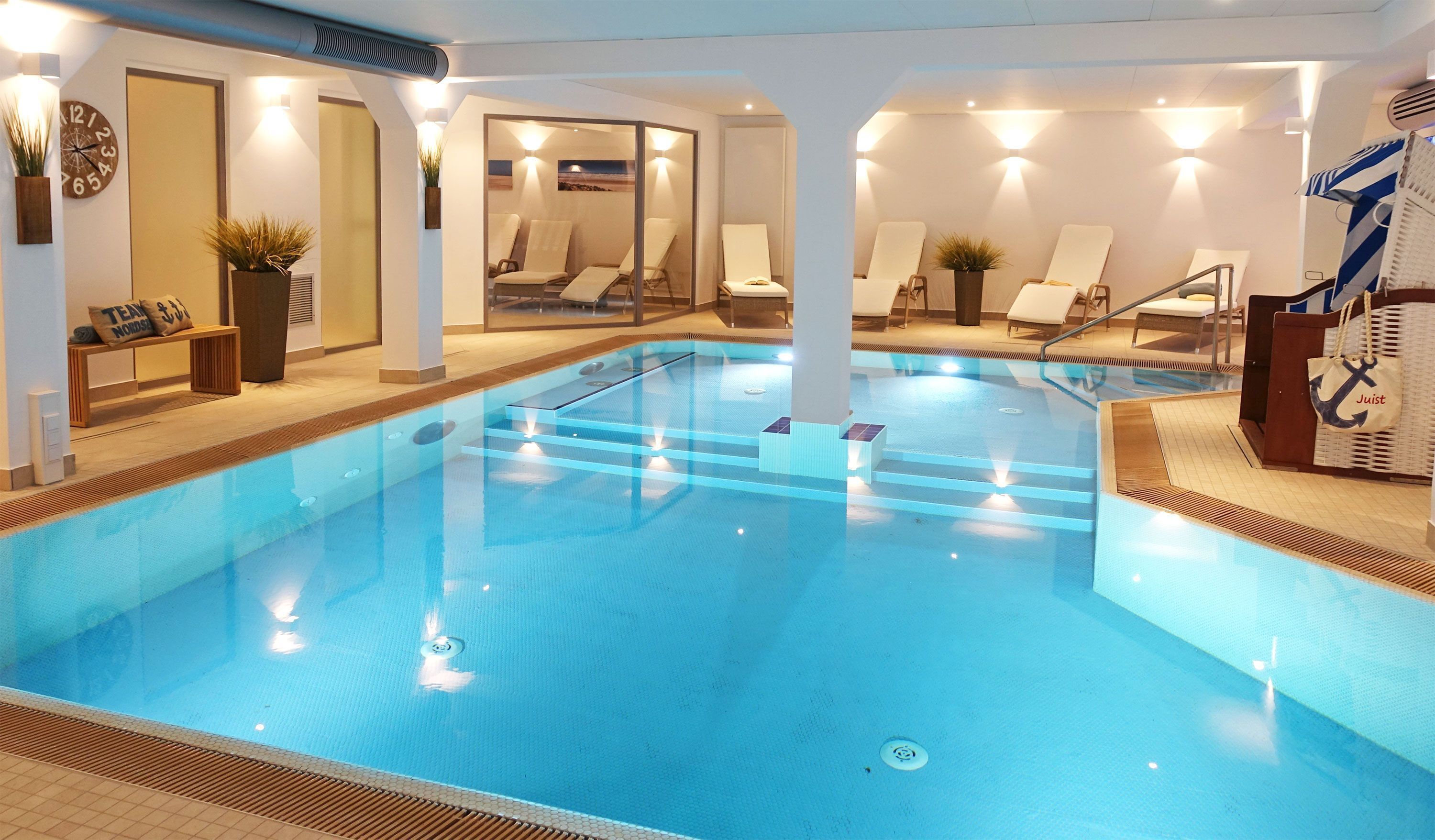 Ein Hallenbad mit klarem Wasser, Liegestühlen und einer Uhr an der Wand.