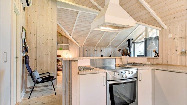 A compact kitchen with a built-in oven, a dining area with a chair, and wooden walls. - Awesome home in Oksbøl with sauna (Oksbøl)