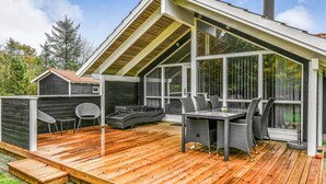 A covered outdoor patio with a wooden deck, a dining table with chairs, and a small seating area. - Awesome home in Oksbøl with sauna (Oksbøl)