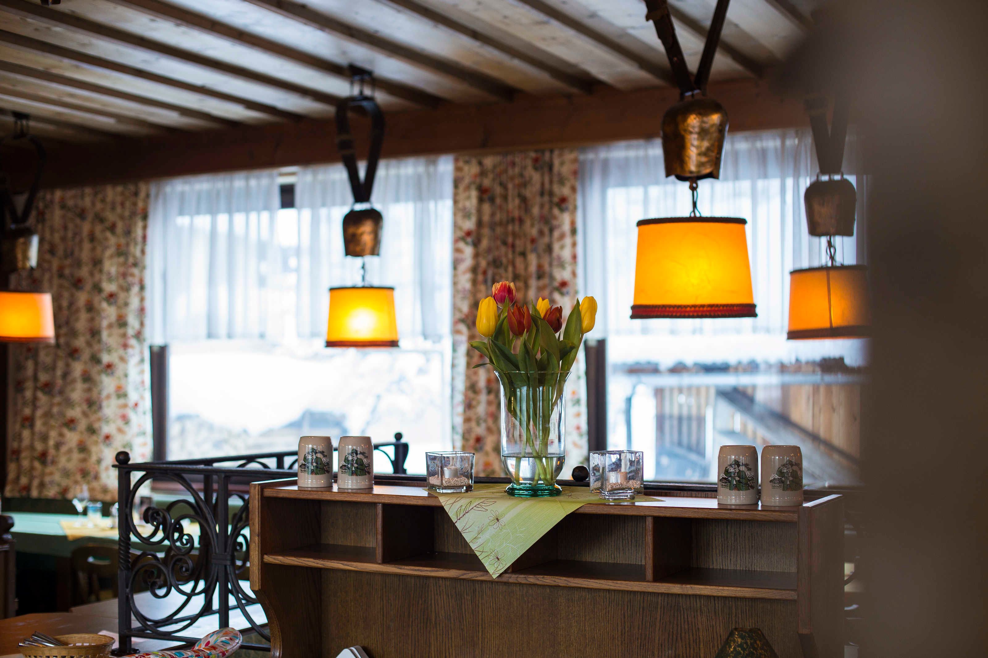 Un comptoir d’accueil en bois, agrémenté d’un vase de tulipes, de lampes suspendues et offrant une vue sur les montagnes par la fenêtre.