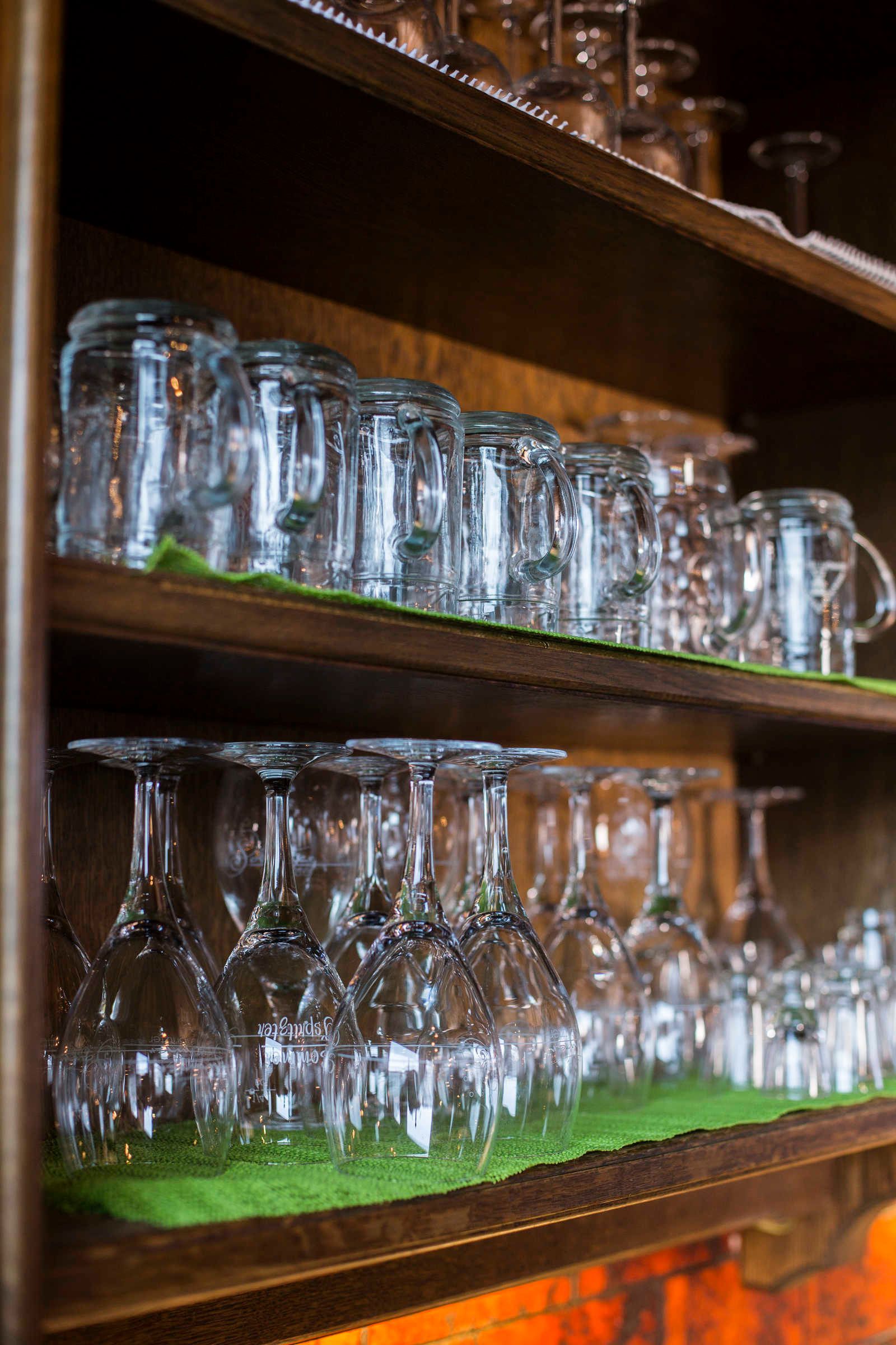 A wooden shelf with multiple glassware items, including wine glasses and tumblers, arranged on a green cloth.
