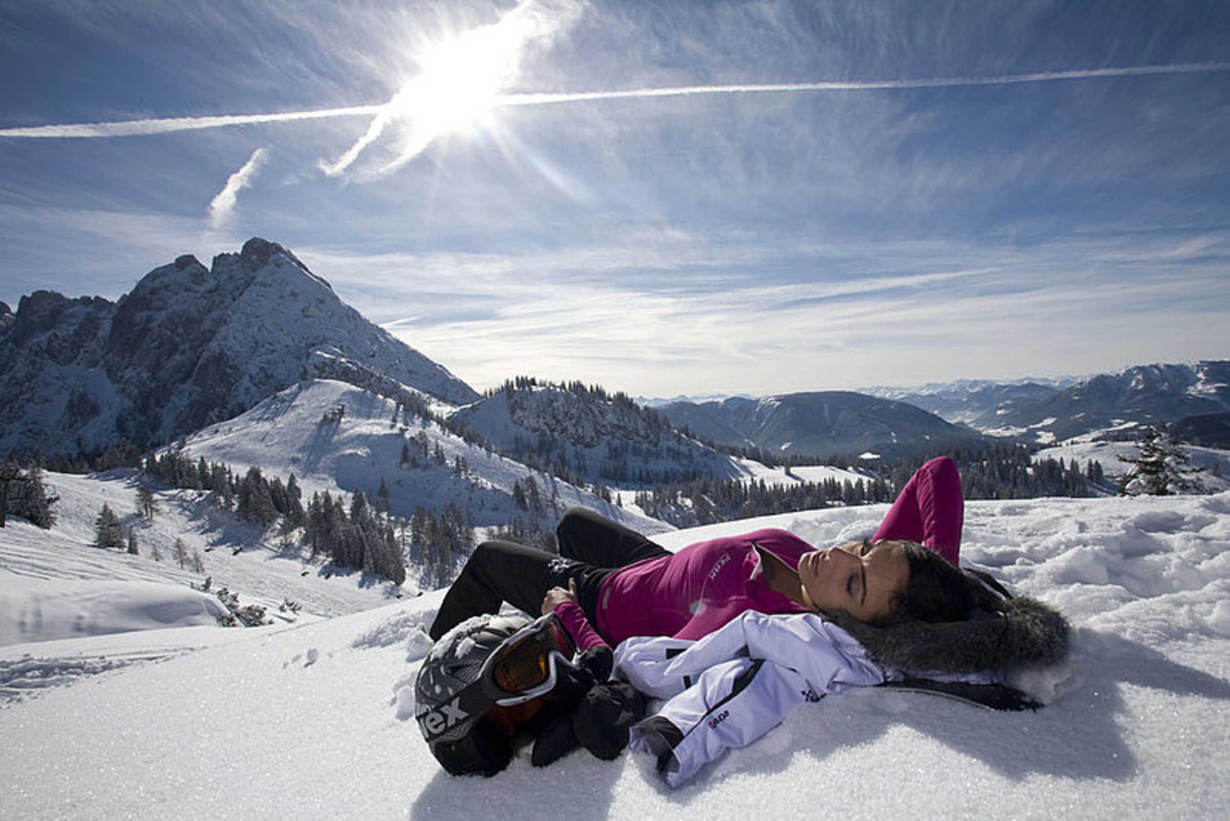 A person lying on snow-covered ground with mountains in the background.