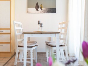 Un coin repas avec une table et des chaises blanches, un tableau au-dessus de la table et une fenêtre avec des rideaux.